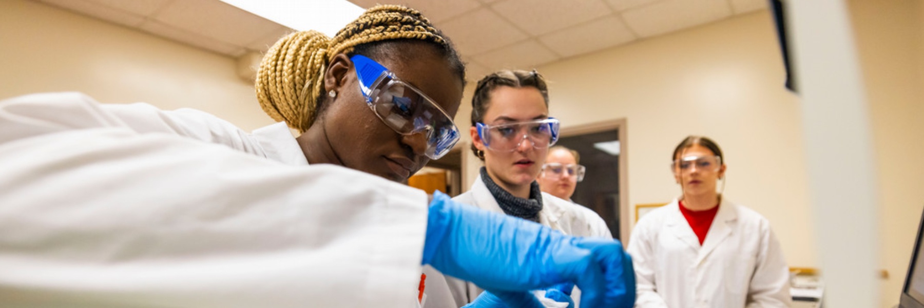 A student puts a test vial into a machine while others look on in a lab at IU South Bend. 